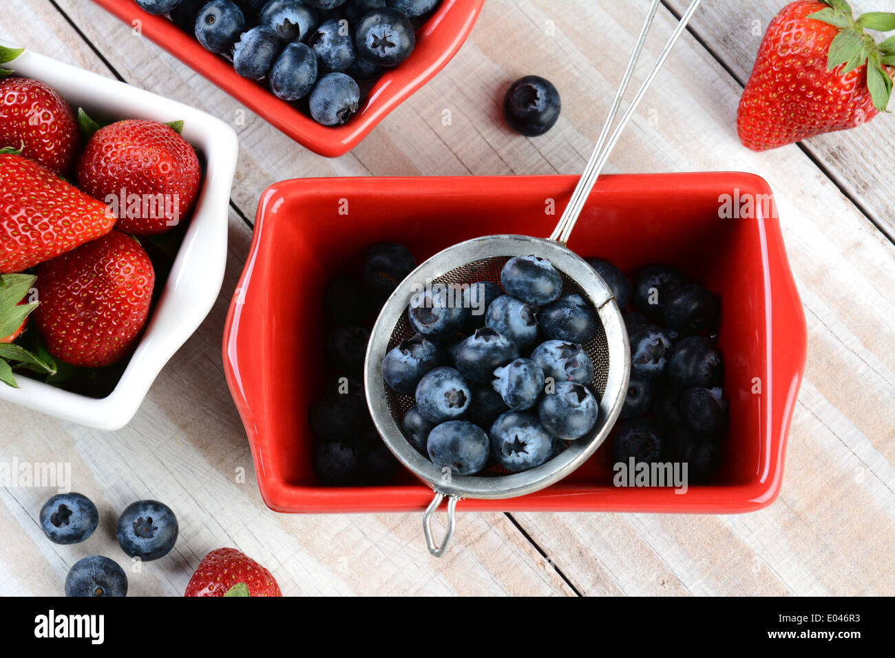 High angle shot of fresh fruits cueillis en rouge et blanc, bols et une crépine. Les fraises et les bleuets Banque D'Images