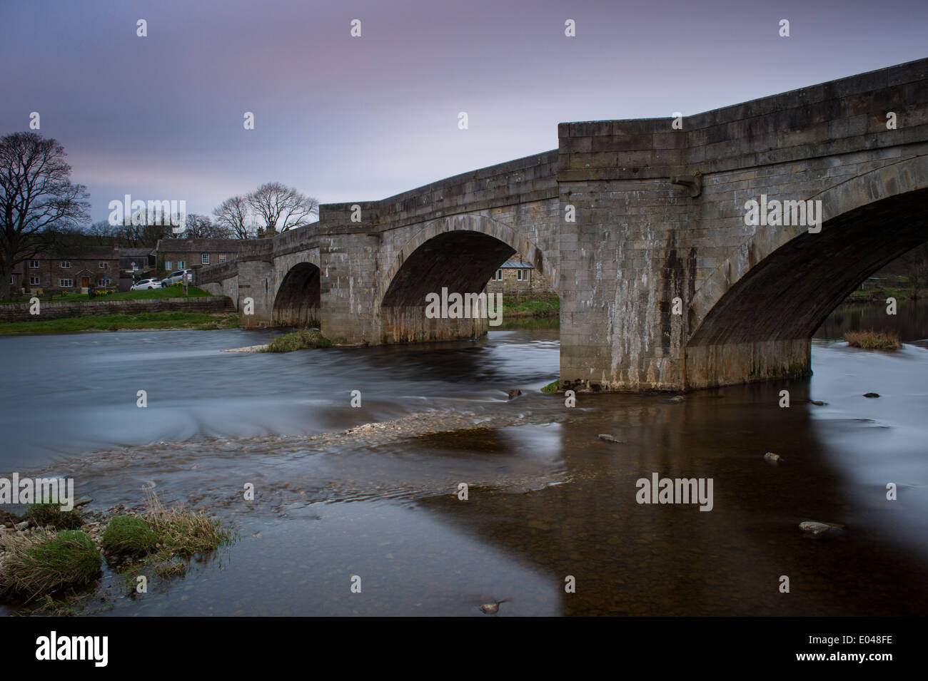Vue de pont en pierre enjambant la rivière Wharfe circulant dans Tonbridge village sur une soirée dans le cadre de printemps rose bleu ciel - Vallées du Yorkshire, England, UK. Banque D'Images