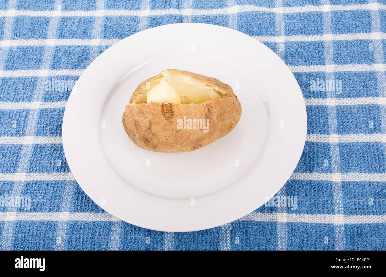 Une pomme de terre au four avec une noix de beurre sur une assiette blanche et bleue serviette Banque D'Images