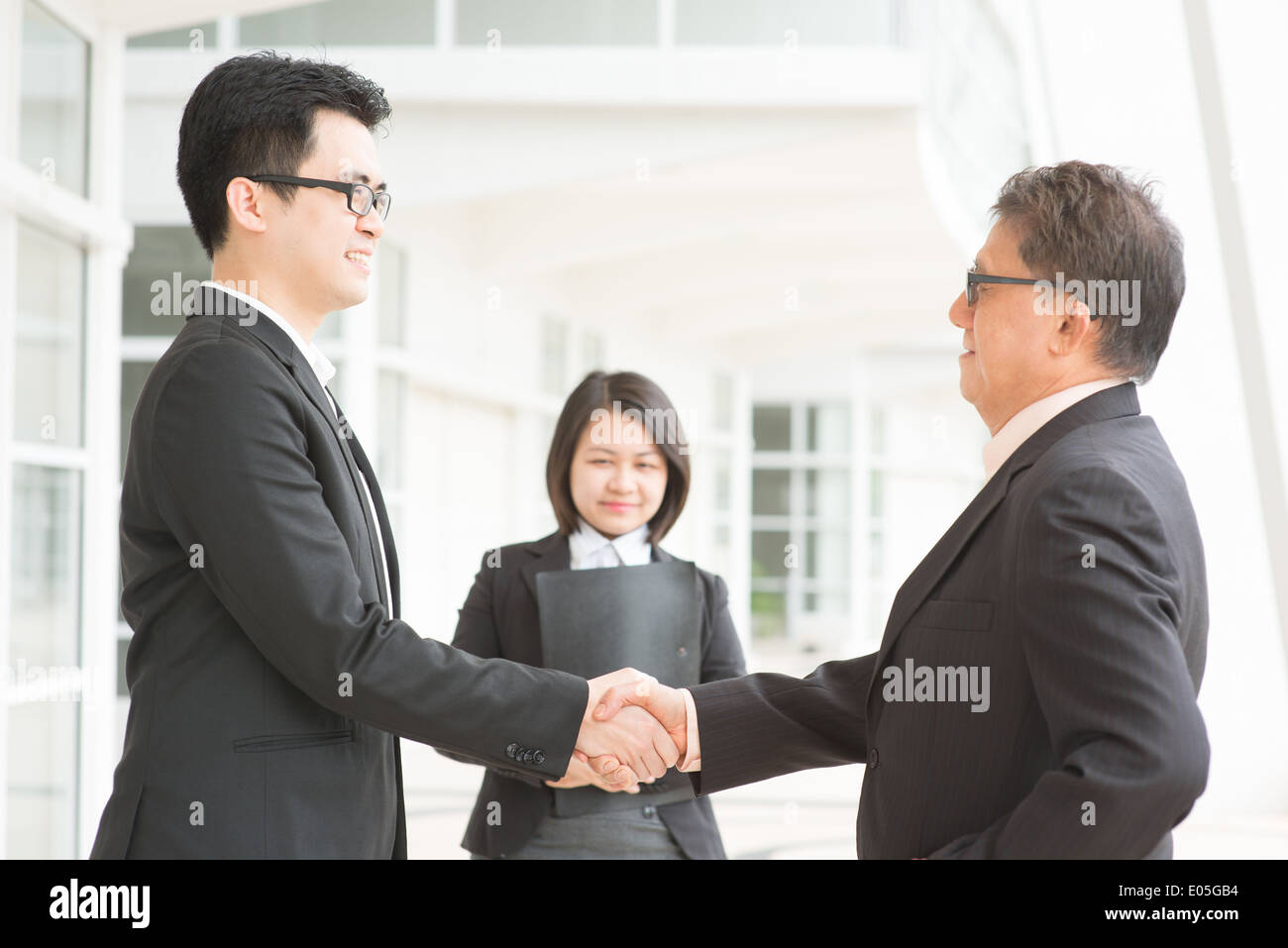 Transaction commerciale, d'affaires de l'Asie l'établissement de liaison. Chef principal part agiter avec de jeunes dirigeants. Immeuble de bureaux moderne architecture. Banque D'Images