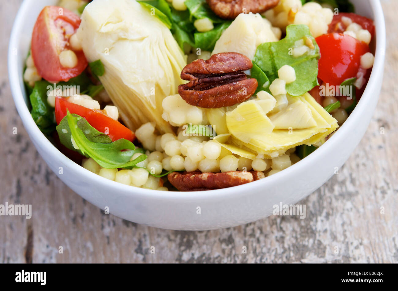 Une salade rafraîchissante avec des coeurs d'artichaut, grand couscous (couscous) Jérusalem, feuilles argula, tomates cerises et pacanes grillées. Banque D'Images