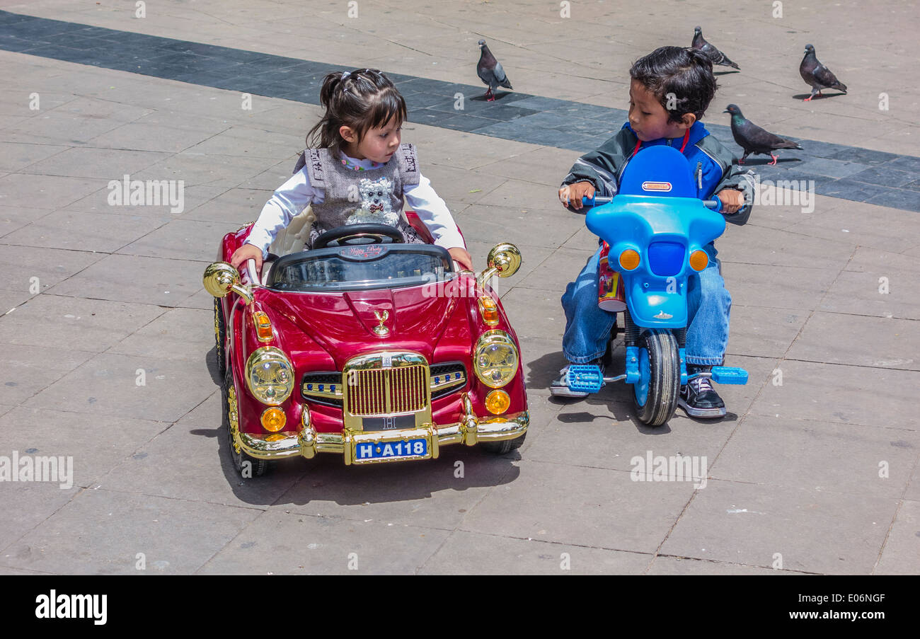 Une fille est assise dans son bolivien très fantaisie jouet voiture à télécommande qui est admiré par un garçon plus pauvres en sucre, Bolivie. Banque D'Images