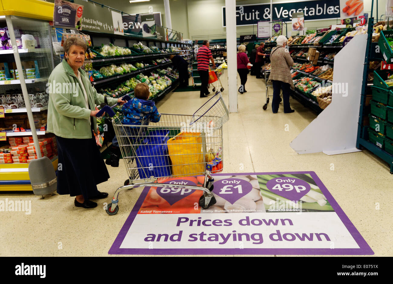 Une vieille dame shopping dans supermarché Tesco, poussant un chariot sur un plancher panneau annonçant des prix bas Banque D'Images