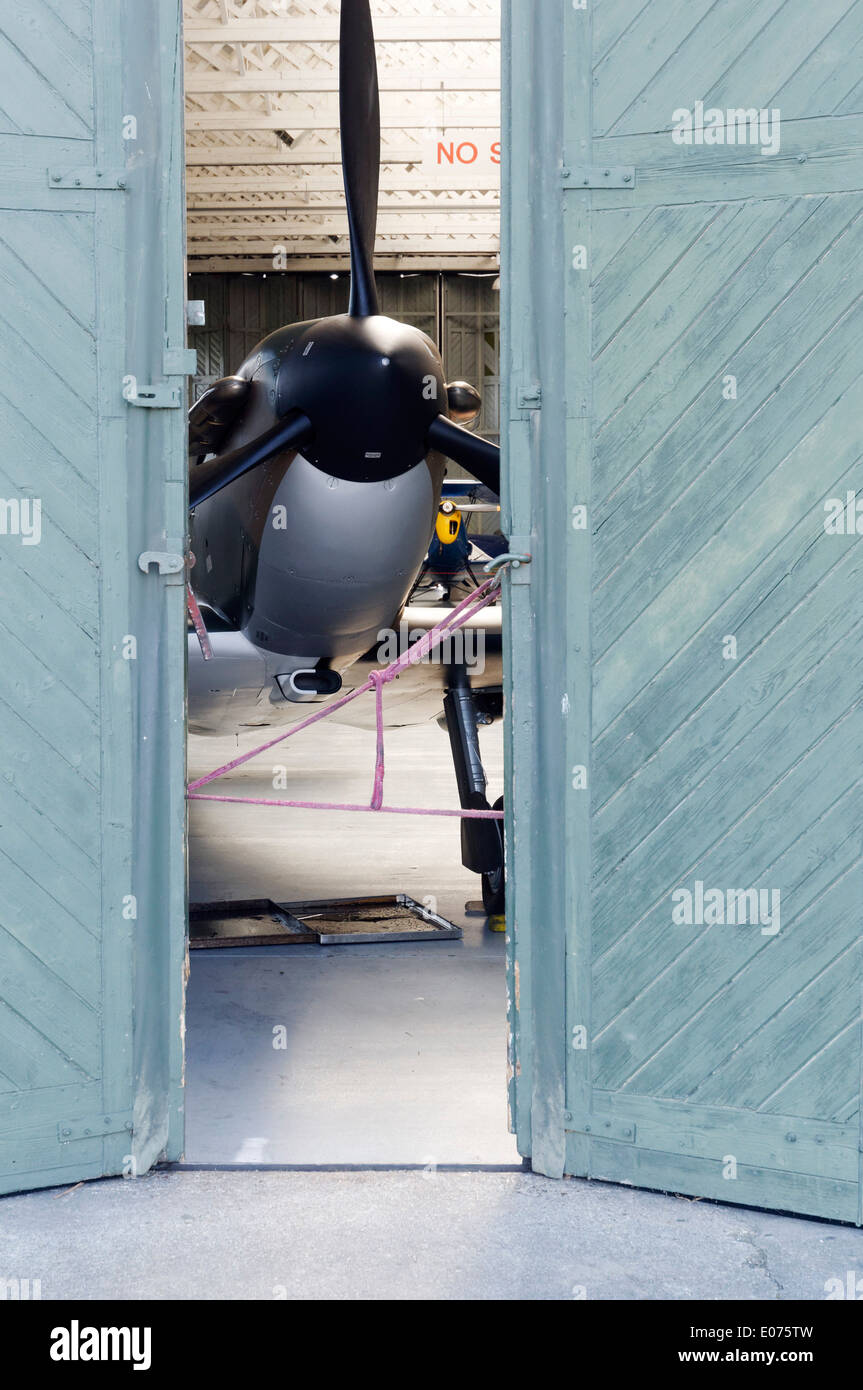 Un Supermarine Spitfire avion de chasse à l'intérieur partiellement ouvert portes du hangar dans la restauration boutique à Duxford Air Museum, Angleterre Banque D'Images