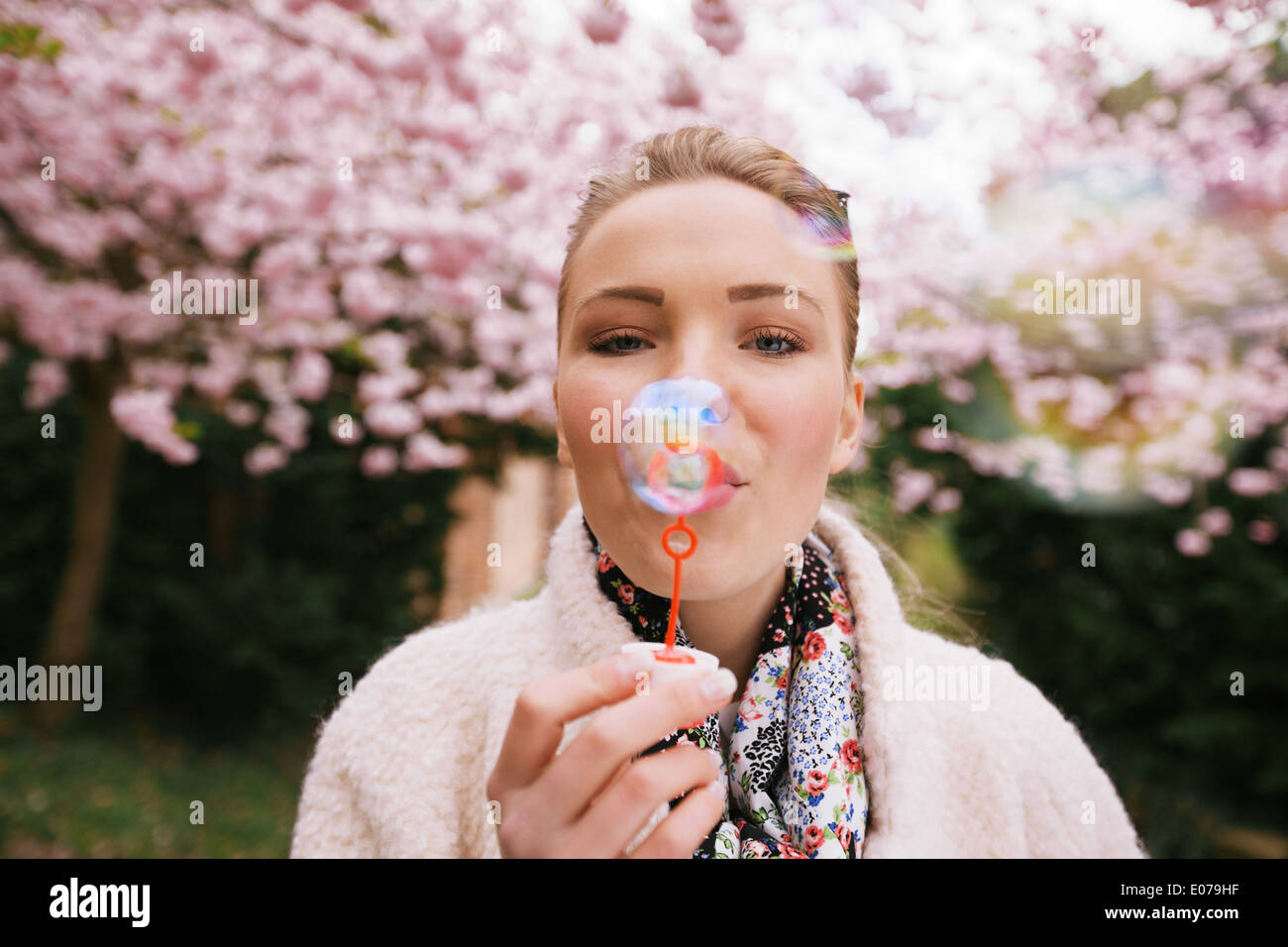 Portrait de belle jeune femme faisant des bulles au parc. Joli modèle féminin avec bulle baguette sur le jardin en fleurs au printemps. Banque D'Images