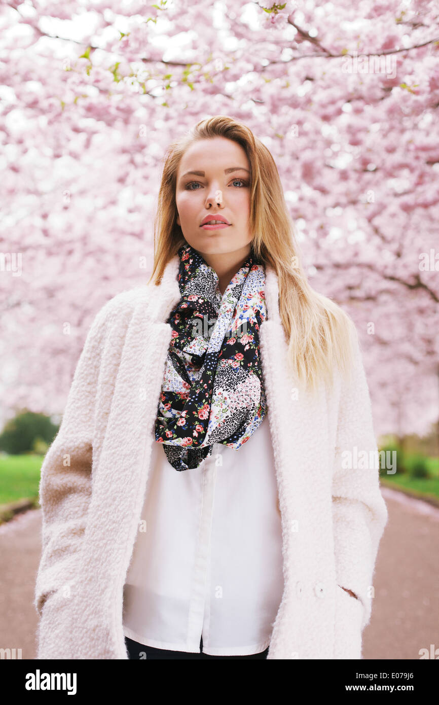 Jeune femme portant manteau et écharpe au printemps. Jeune modèle féminin chez spring blossom park. Banque D'Images