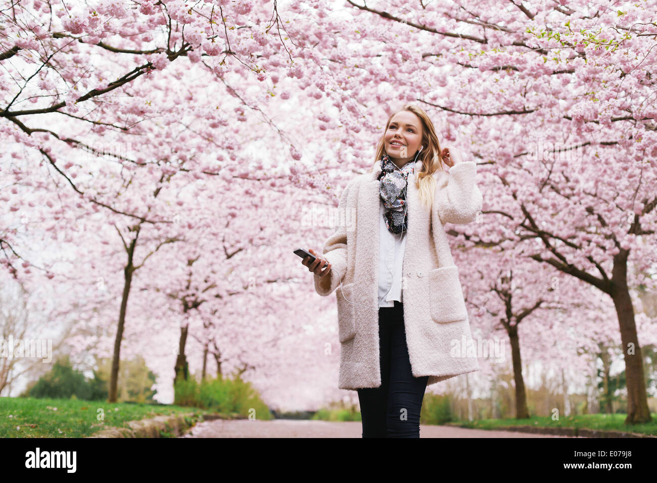 Smiling young woman listening to music in park. Belle jeune femme à fleur de printemps jardin. Banque D'Images