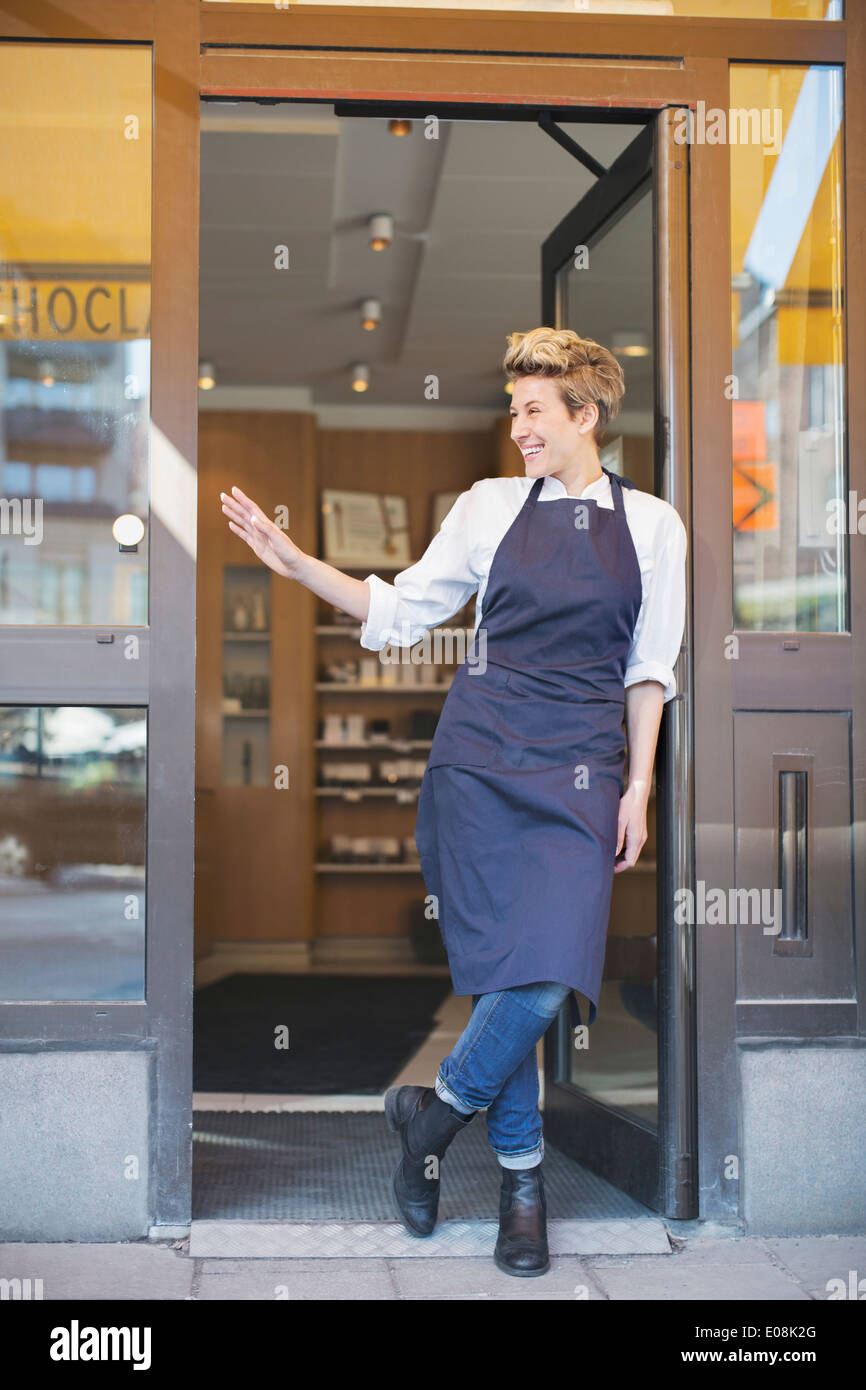 Toute la longueur de l'heureux propriétaire femme gesticulant debout à l'entrée du café Banque D'Images