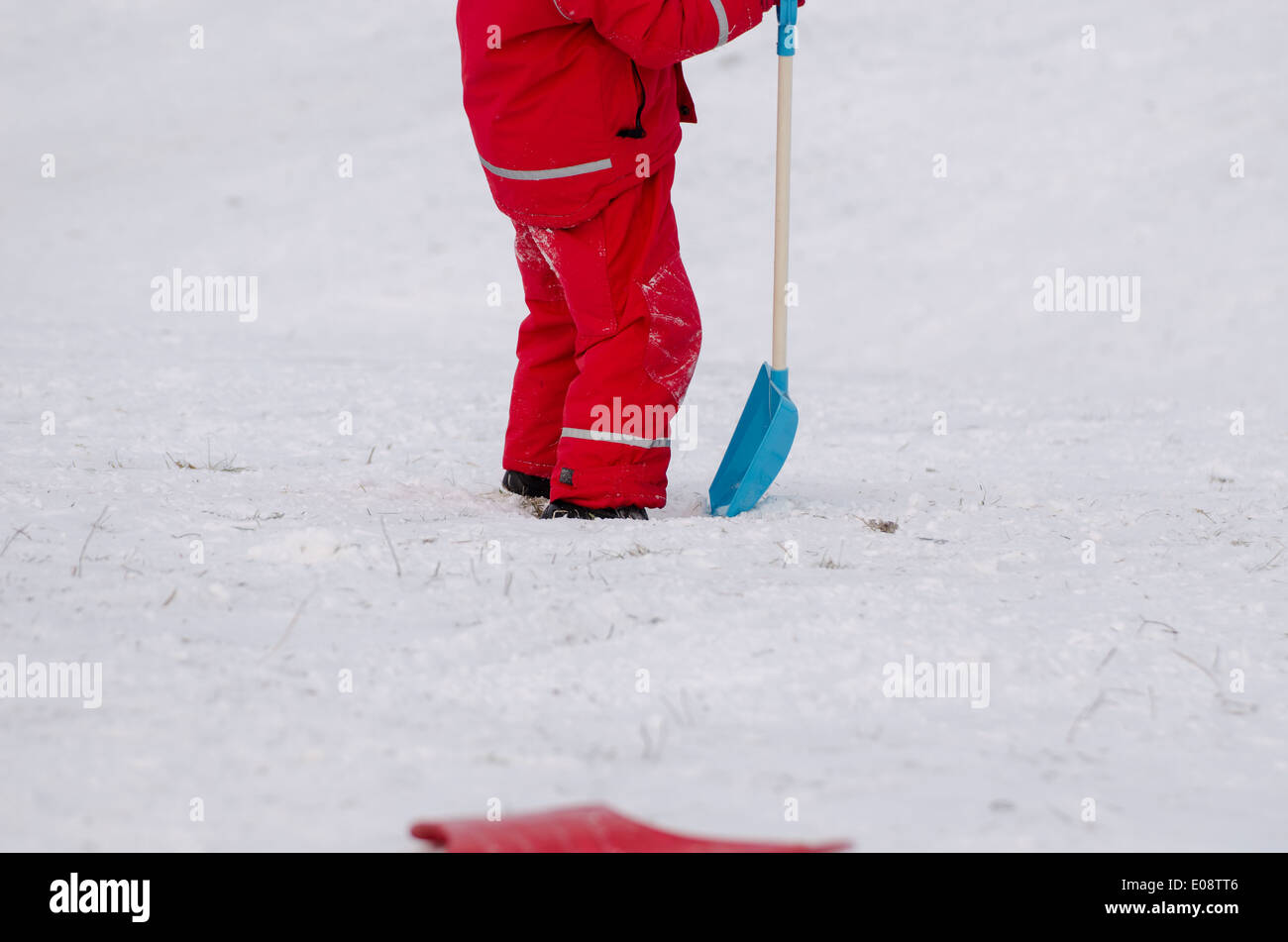 Position de l'enfant avec une grande pelle à neige vêtu de rouge vêtements imperméables outdoor en hiver Banque D'Images