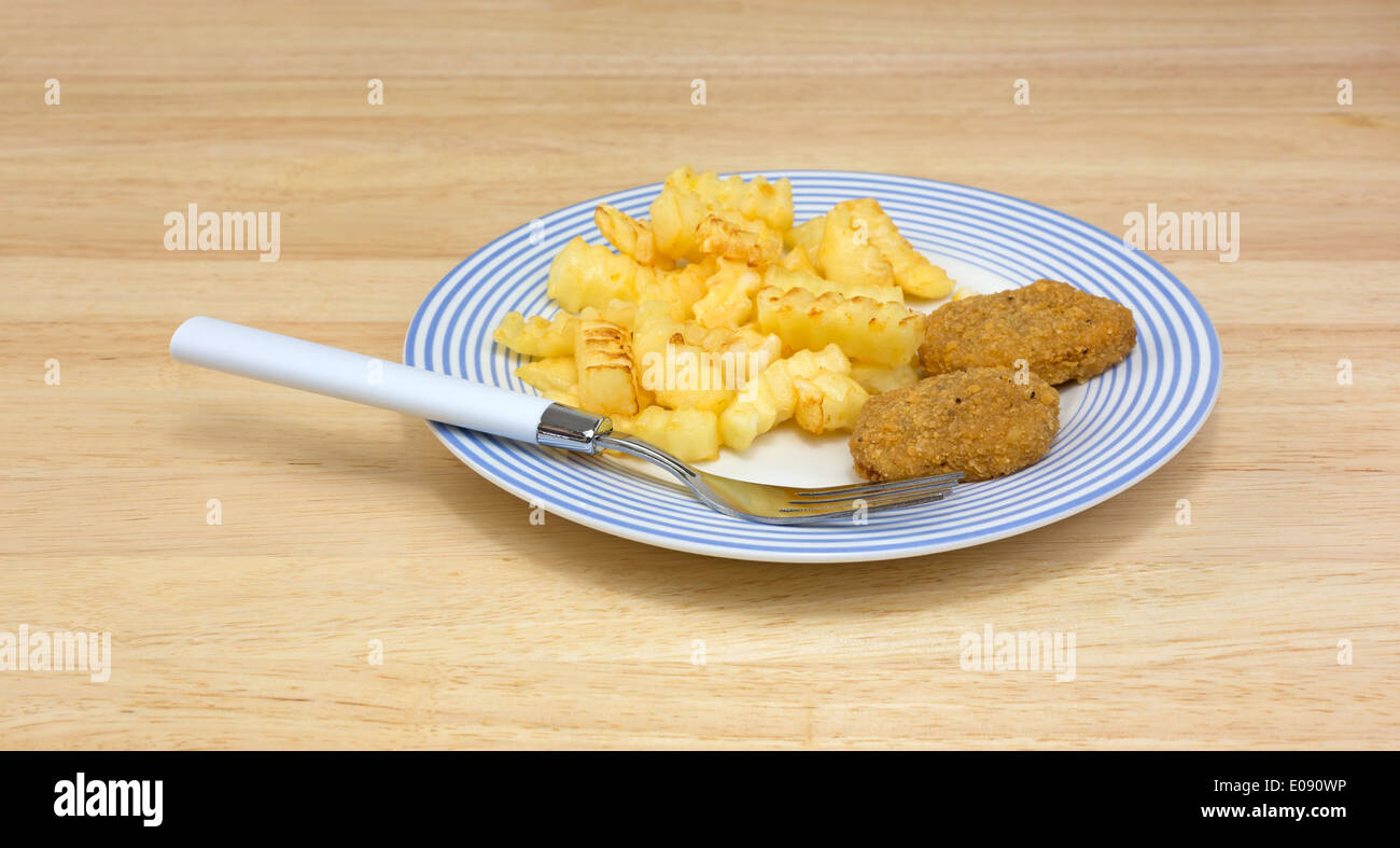 Une assiette de croquettes de poulet avec frites et une fourchette sur une table à manger. Banque D'Images