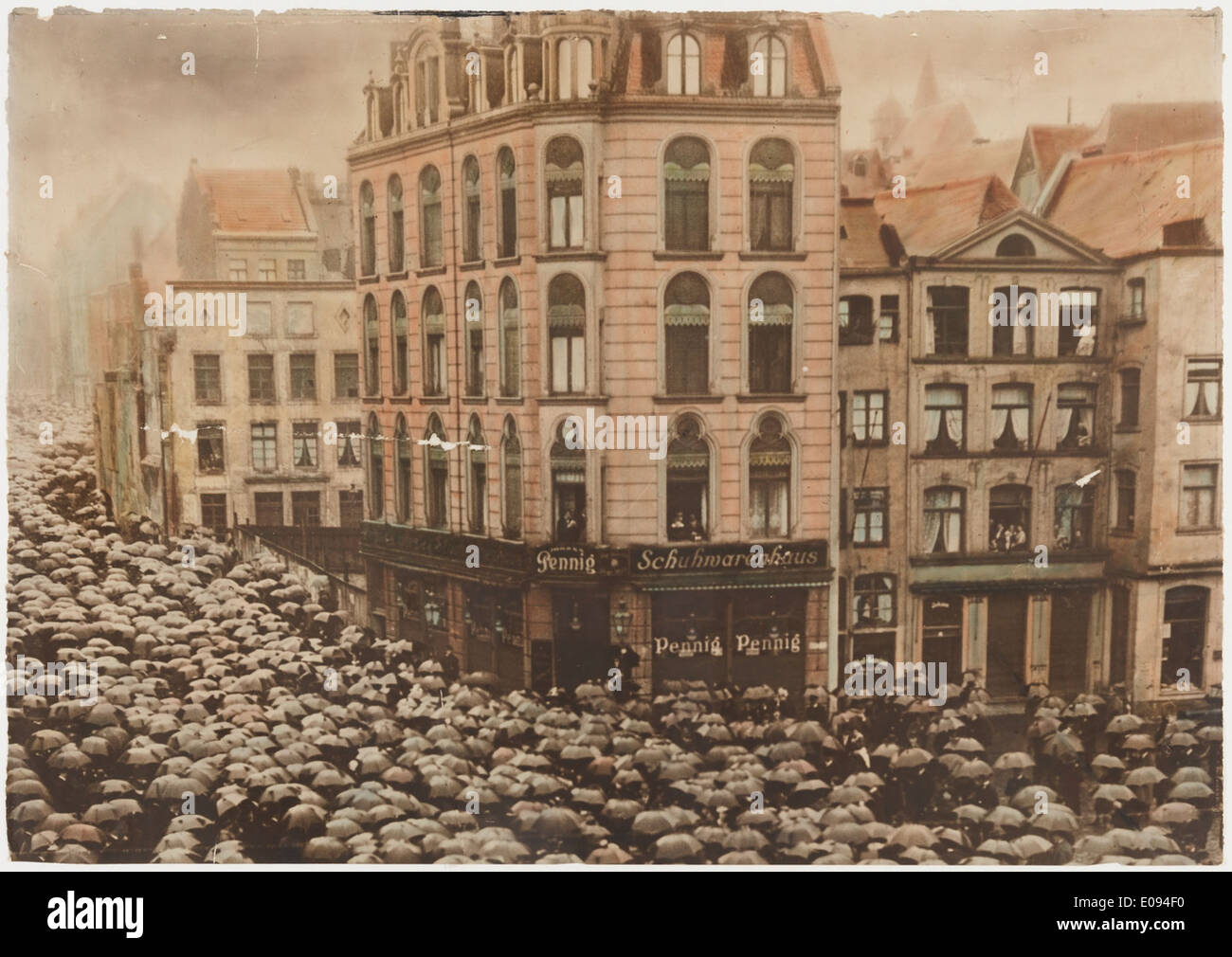 Une photo vintage d'une foule allemande avec des parapluies, représentant des gens dans un rassemblement public. L'image capture l'ambiance d'une époque antérieure, mettant en évidence les moments culturels et historiques. Banque D'Images
