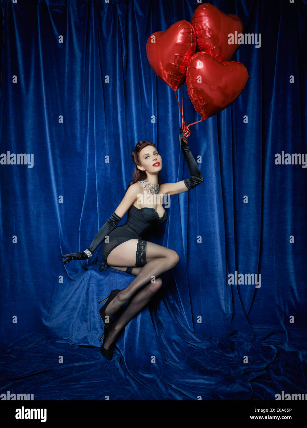 Danseuse Burlesque holding red heart-shaped balloons Banque D'Images