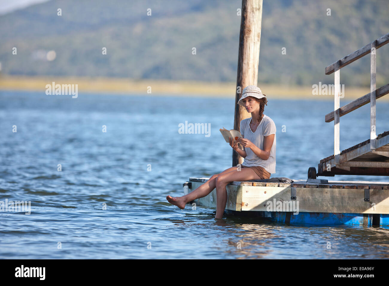 Young woman sitting on Jetty, reading book Banque D'Images