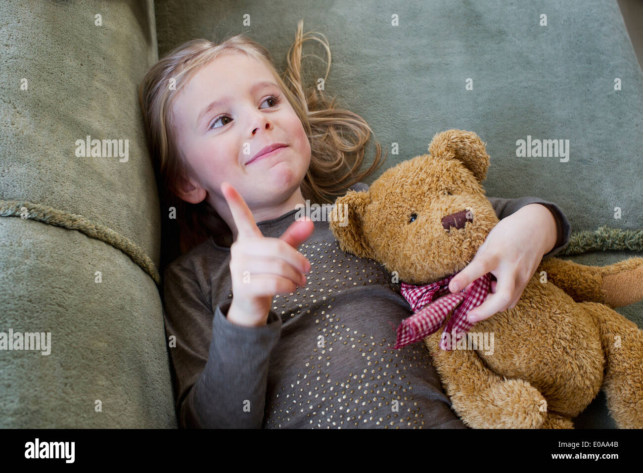 Young Girl lying on sofa avec son ours en peluche Banque D'Images