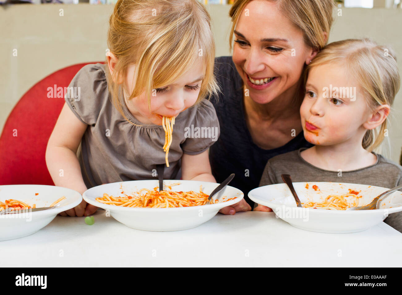 Mid adult mère mange du spaghetti avec ses deux jeunes filles Banque D'Images