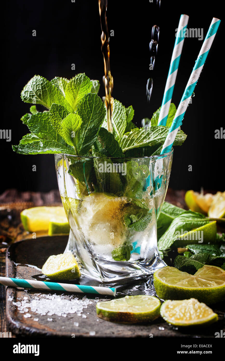 Verre de mojito cocktail Rhum avec bec verseur et le soda, la menthe fraîche, des limes et des cubes de glace sur fond noir. Banque D'Images