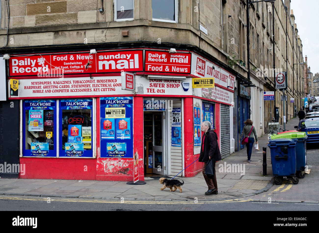 Un homme promène son chien au-delà d'un corner shop dans la région d'Édimbourg Fountainbridge. Banque D'Images