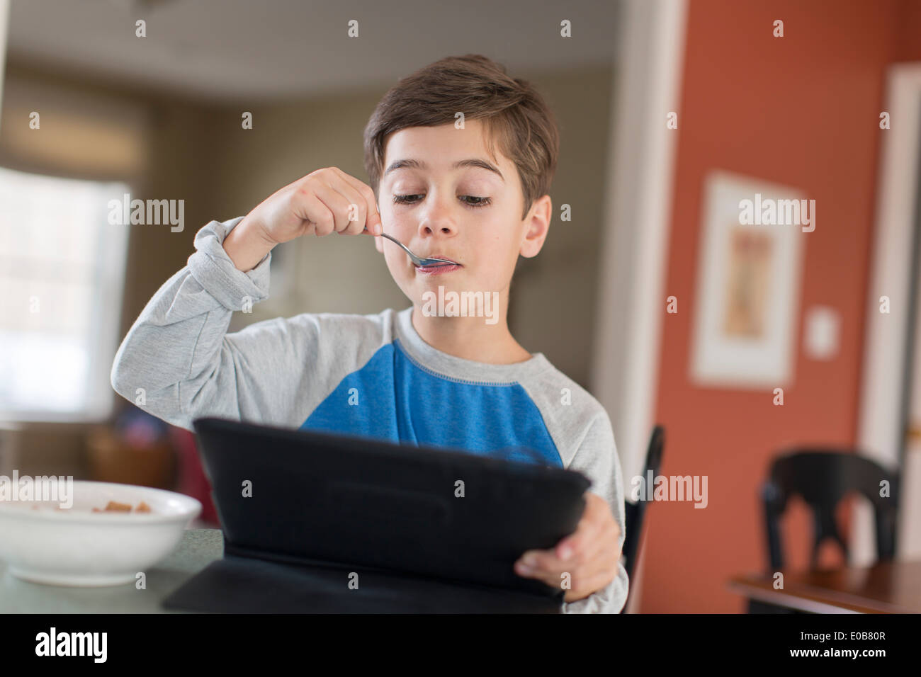 Boy looking at digital tablet tout en prenant un petit déjeuner Banque D'Images
