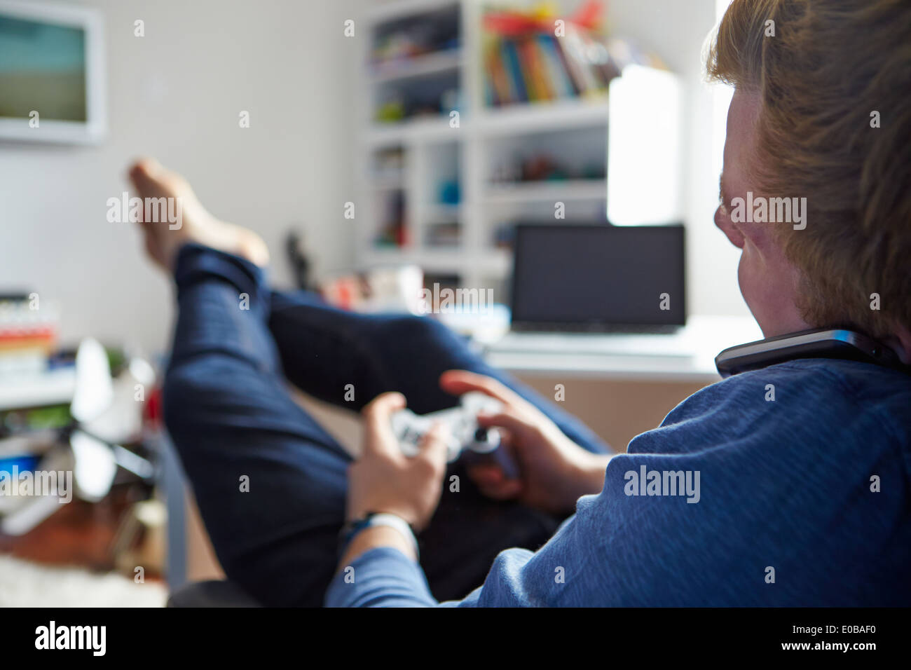 Teenage Boy Playing Video Game et Talking On Mobile Phone Banque D'Images