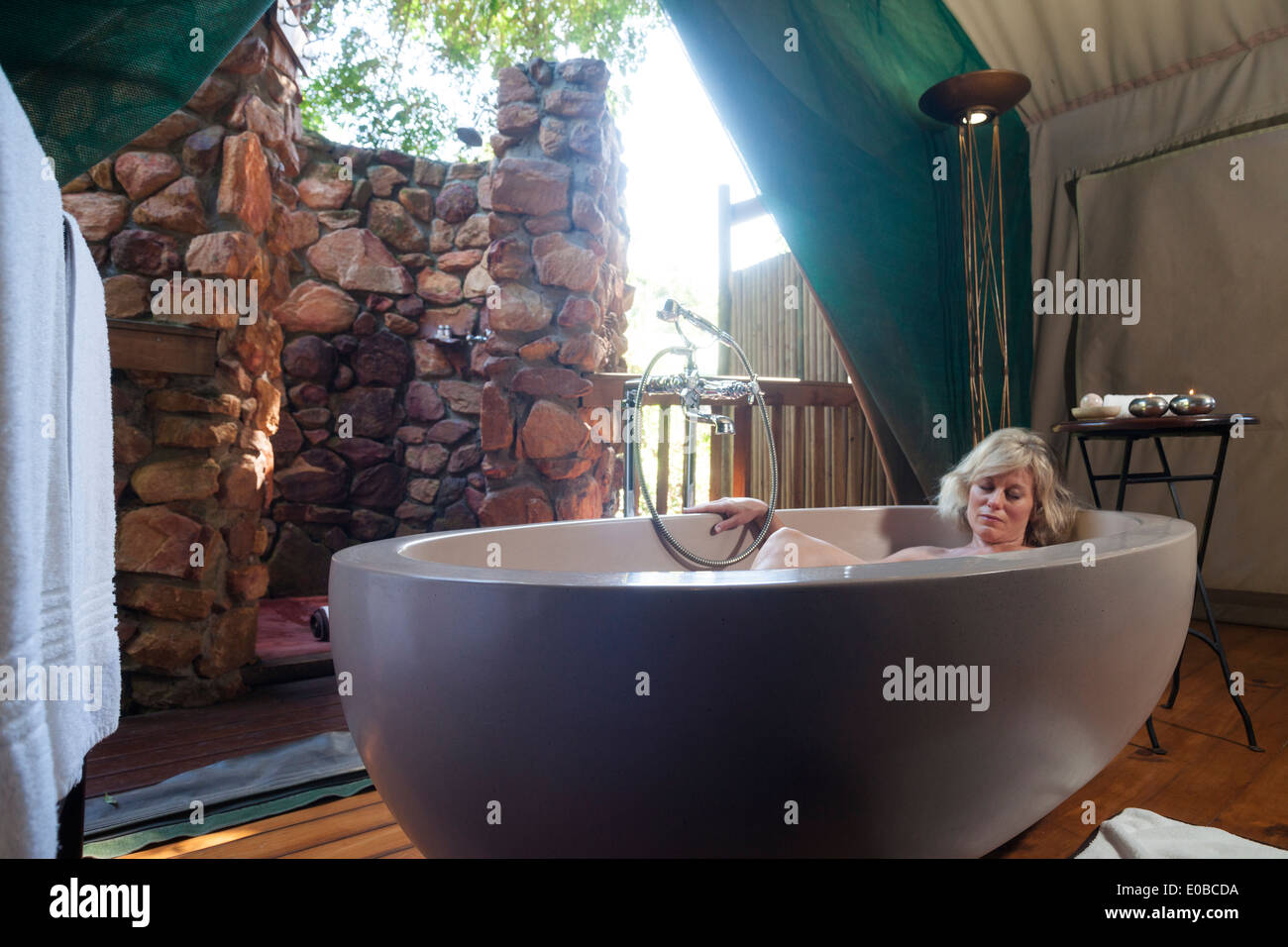 Femme blonde pan au sein d'une grande baignoire ovale dans une tente safari de luxe, Botlierskop Game Lodge, Mosselbay, Afrique du Sud Banque D'Images