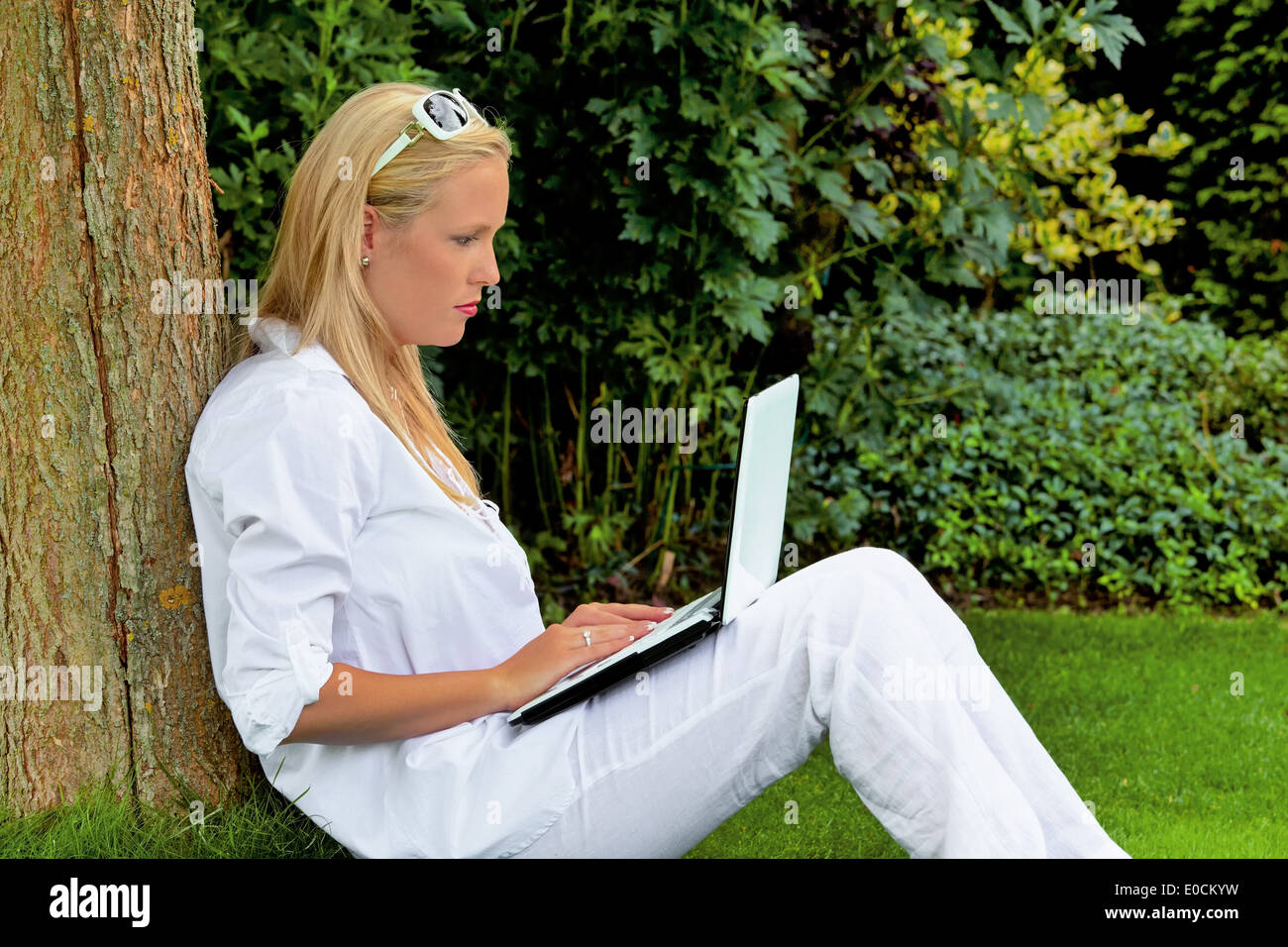 Une jeune femme est assise avec un ordinateur portable dans le jardin et surfe sur l'Internet Banque D'Images