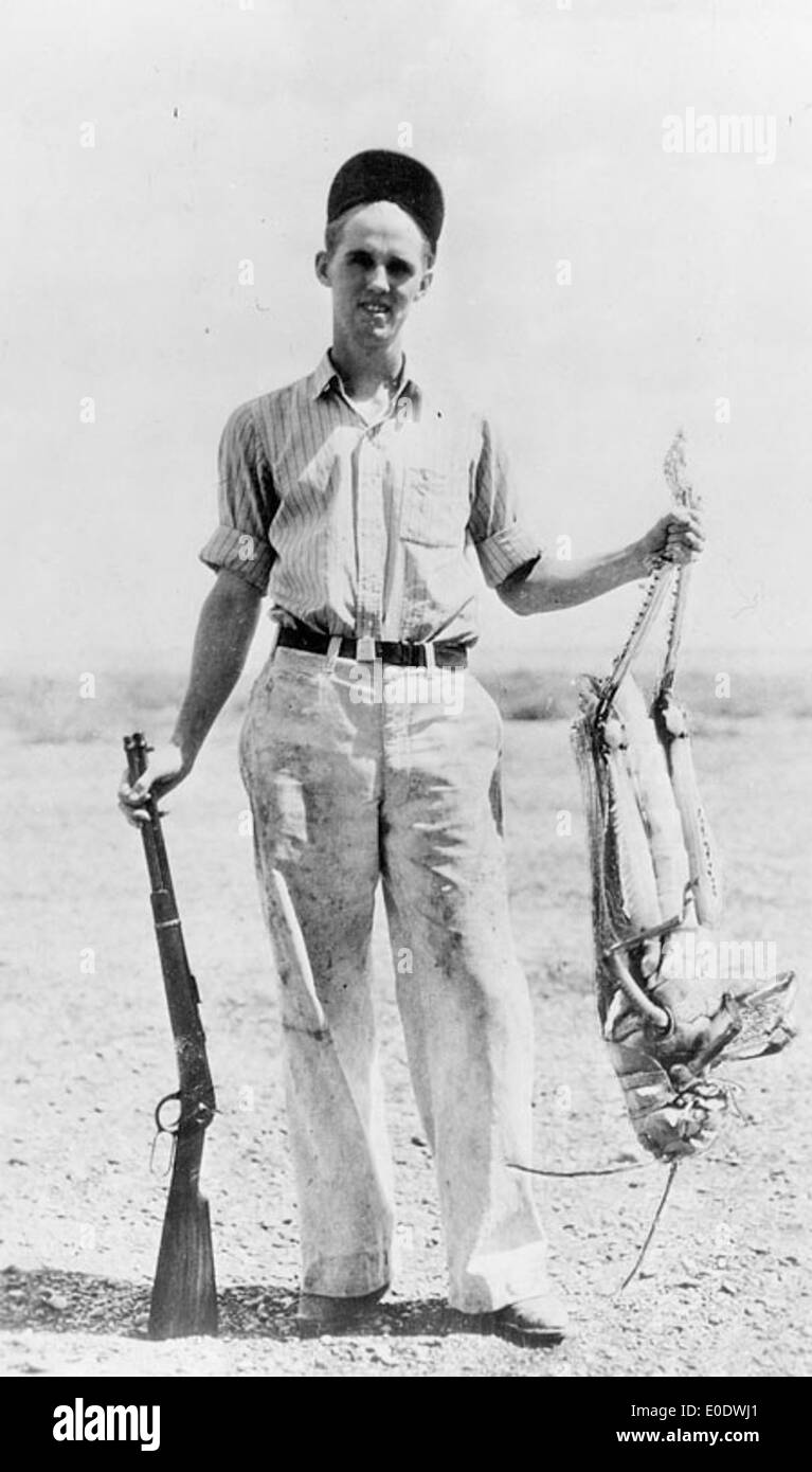 Un chasseur se tient debout avec une grande sauterelle prise dans les années 1930, mettant en évidence un moment insolite et divertissant lors d’une aventure en plein air. Cette image capture une ère d'exploration et de découverte. Banque D'Images