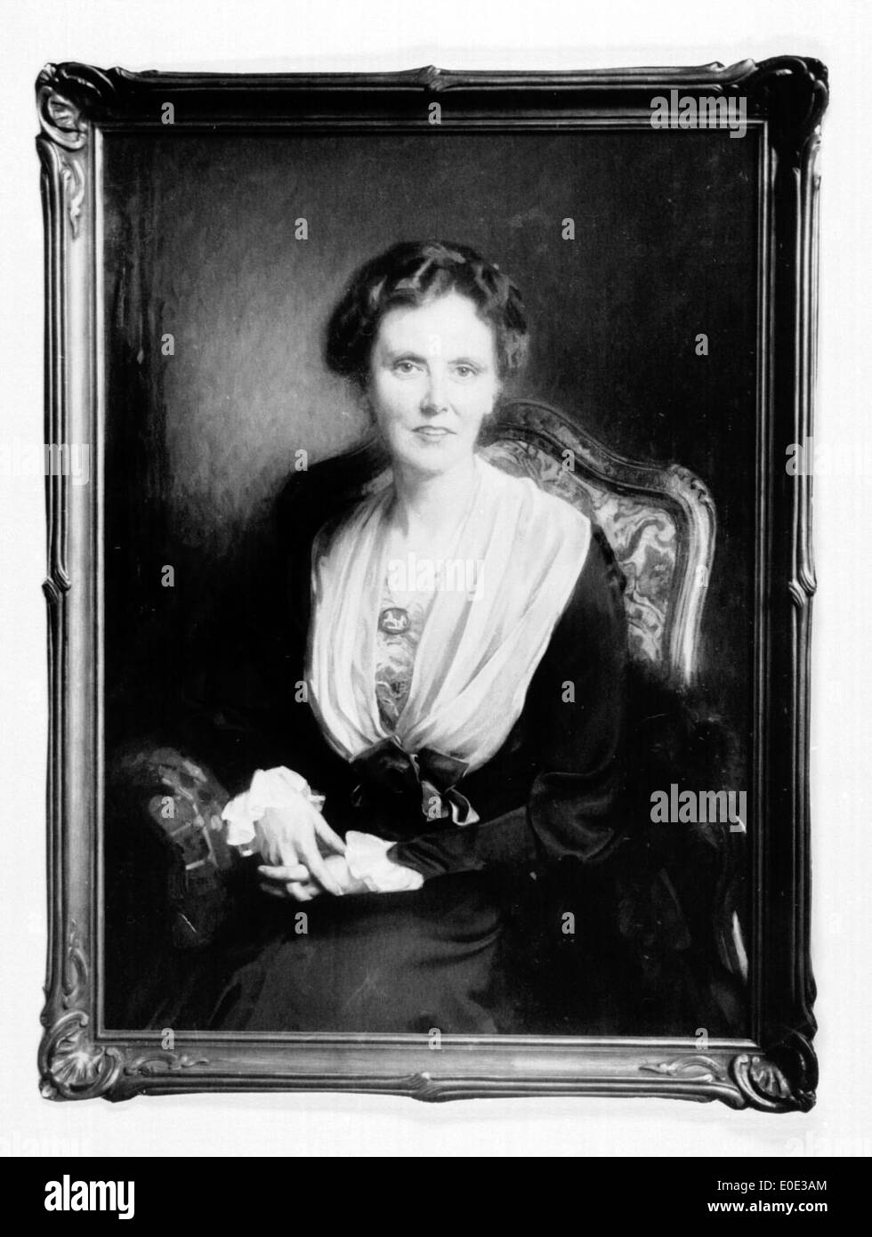 Portrait en noir et blanc d'une femme assise sur une chaise, peut-être pris au début du XXe siècle. La photographie présente une pose classique et des vêtements typiques de la période, avec des lieux historiques notables référencés. Banque D'Images