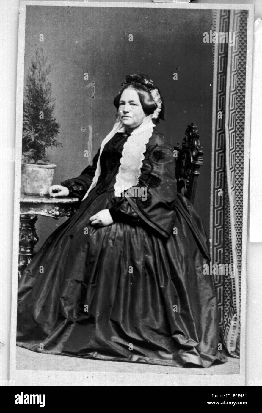 Portrait vintage d'une femme âgée assise à l'extérieur, capturé dans une photographie en noir et blanc du début du XXe siècle. L'image reflète la mode et les tendances sociales de cette époque. Banque D'Images