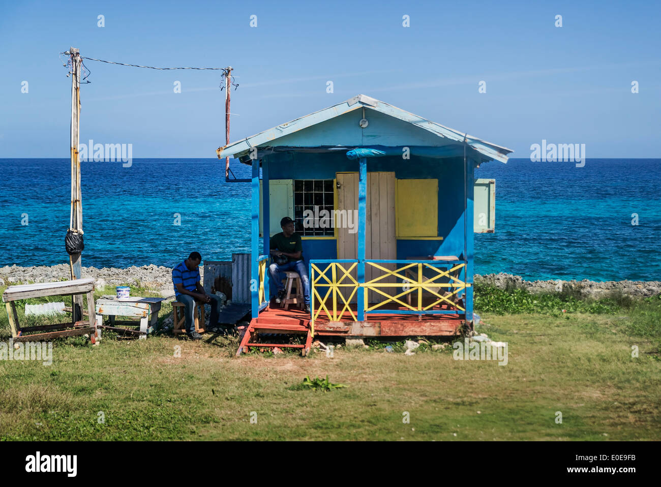 Les hommes de s'asseoir à l'ombre d'une cabane en bord de mer, la Jamaïque Banque D'Images