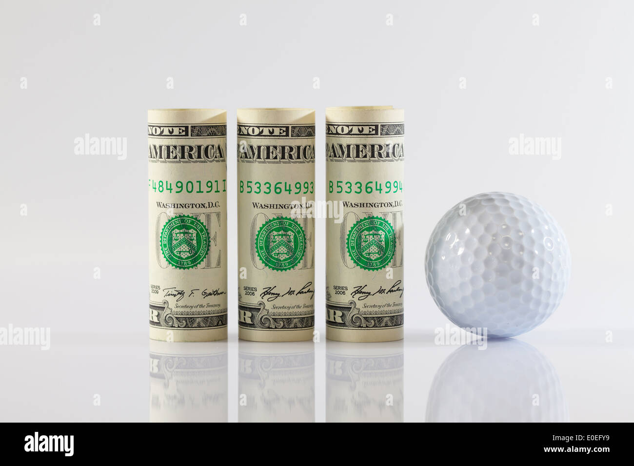 Rouleaux de dollar bills and golff boules sur une table en verre Banque D'Images