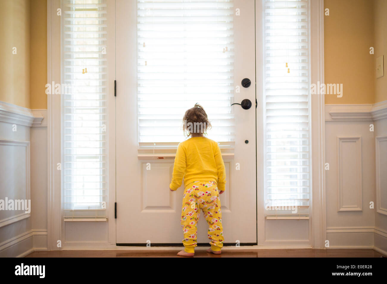 Petite fille en regardant par la fenêtre dans son pyjama. La lumière naturelle. Banque D'Images