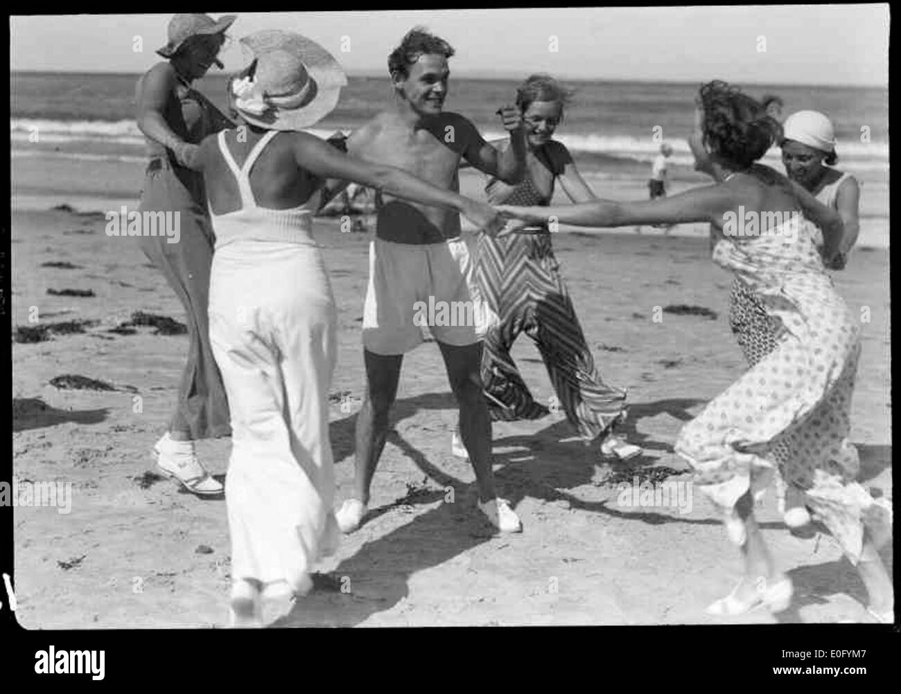 Jeunes sur la plage, capturés dans une photographie en noir et blanc. L'image représente un groupe profitant de leur temps à l'extérieur, s'adonnant éventuellement à des activités de loisirs au bord de la mer. La scène est caractérisée par son cadre naturel de plage. Banque D'Images