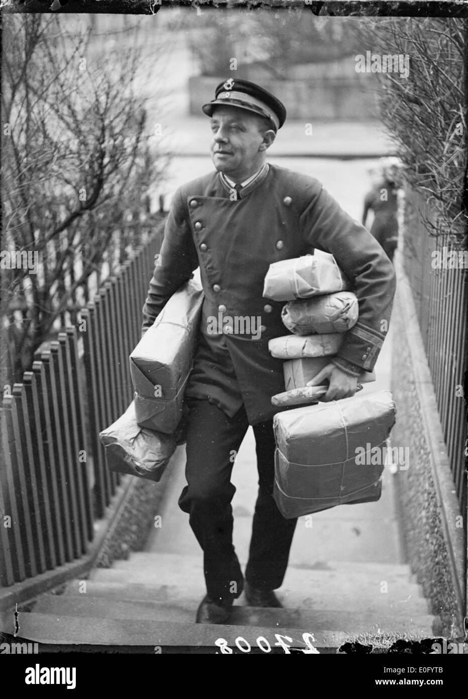 Photographie en noir et blanc représentant la livraison de colis par un facteur à travers un paysage hivernal, avec un sol enneigé et des arbres. Banque D'Images