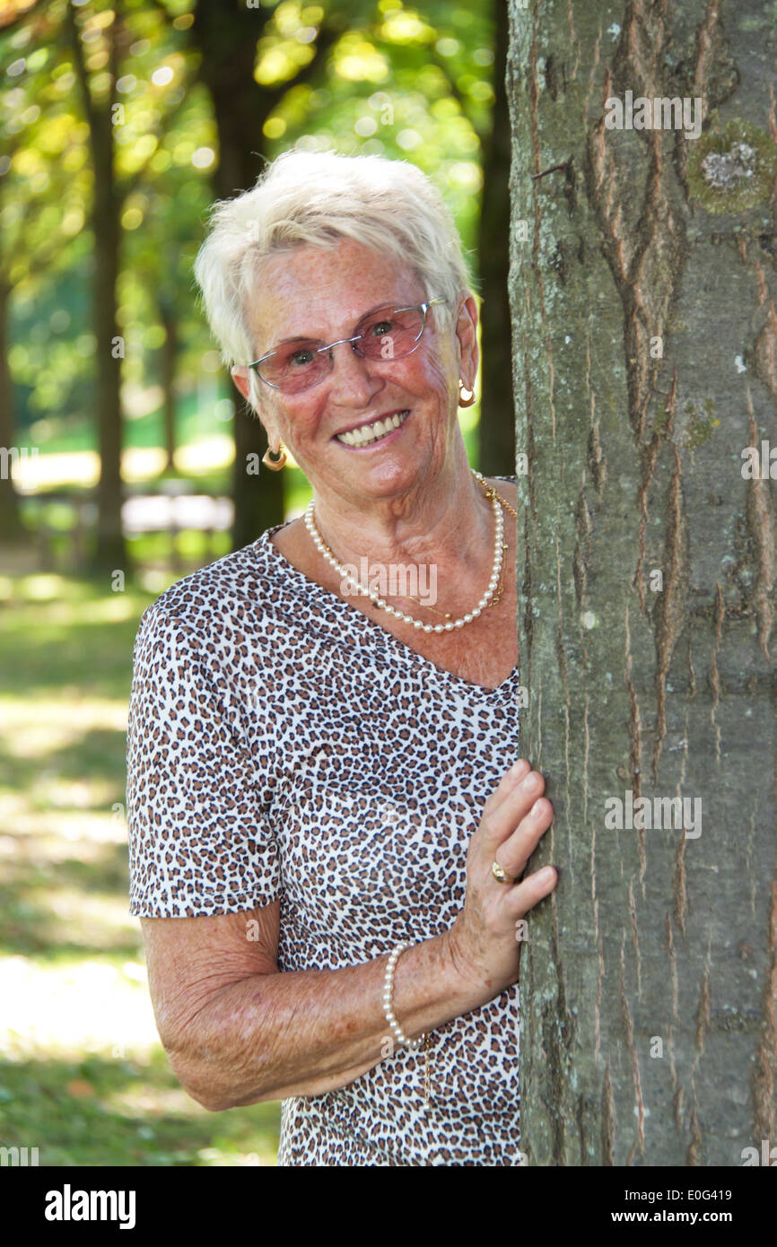 Heureux 74 ans se trouve dans un arbre, Froehliche aeltere Seniorin steht une einem Baum Banque D'Images