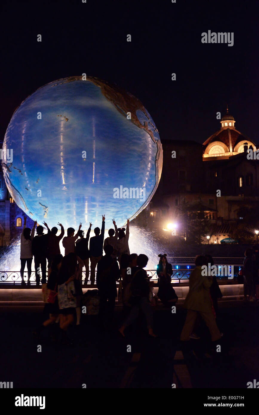 Les enfants posant pour une photo à terre globe fontaine à nuit à Tokyo Disneysea restort Disney theme park, Japon Banque D'Images