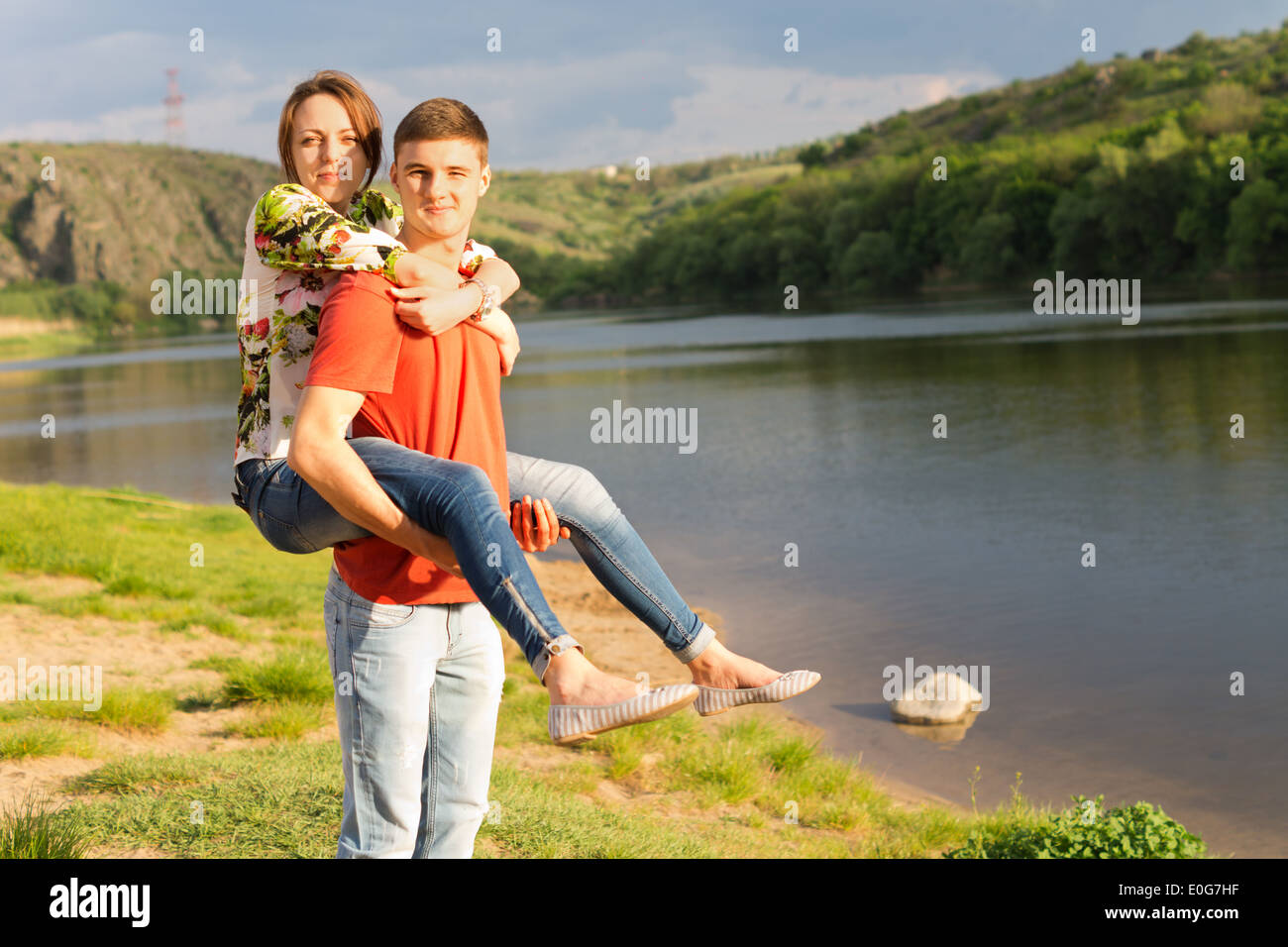 Jeune homme donnant à l'adolescence sa petite amie un piggy back ride le long des rives d'un lac de montagne pittoresque comme ils profitez d'une journée ensoleillée Banque D'Images