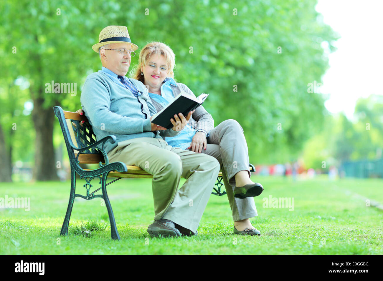 Les personnes âgées de lire un livre assis sur un banc dans le parc Banque D'Images