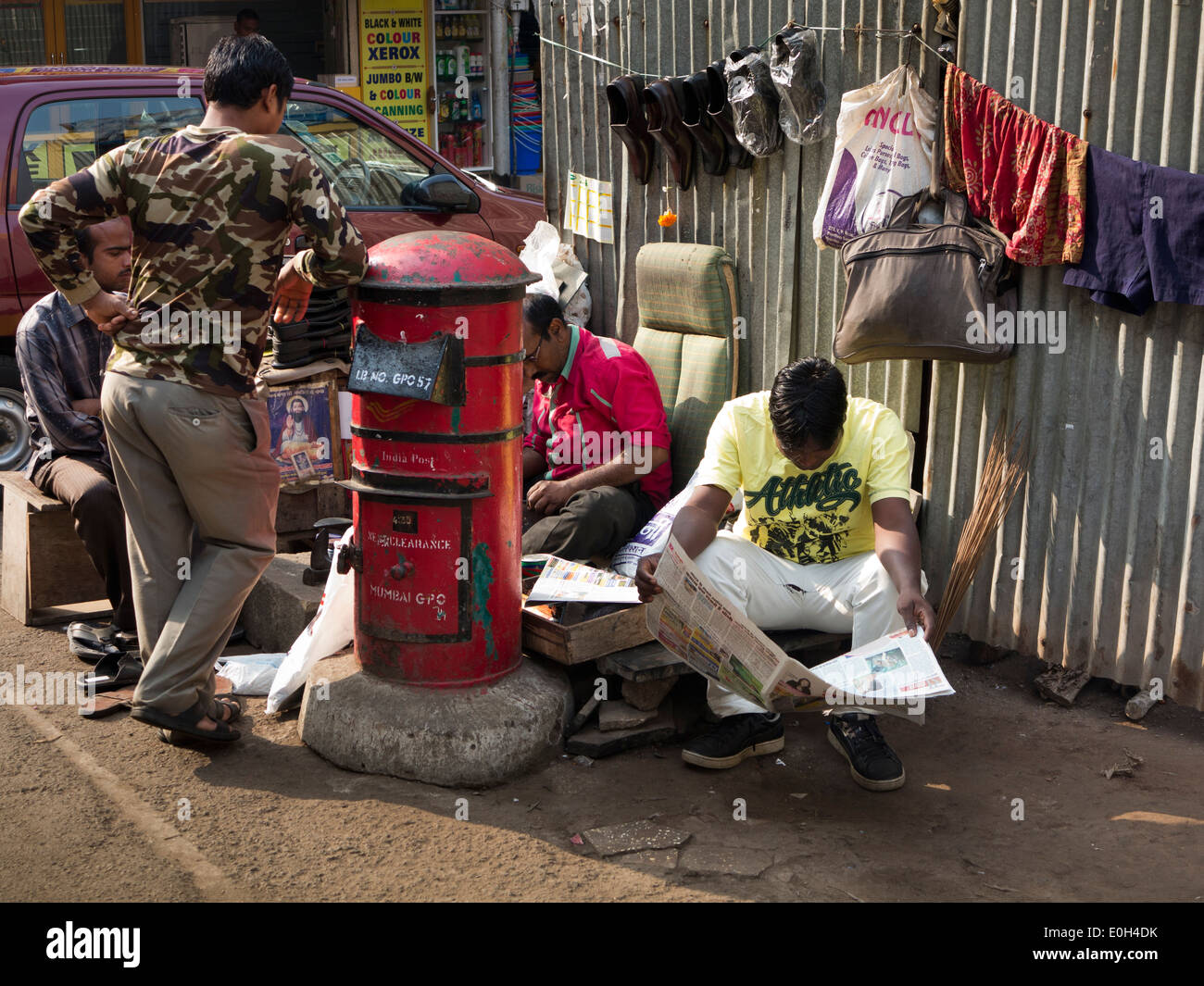 L'Inde, Mumbai, Fort District, les hommes de lire le journal tout en chaussures route chaussures réparations mender Banque D'Images