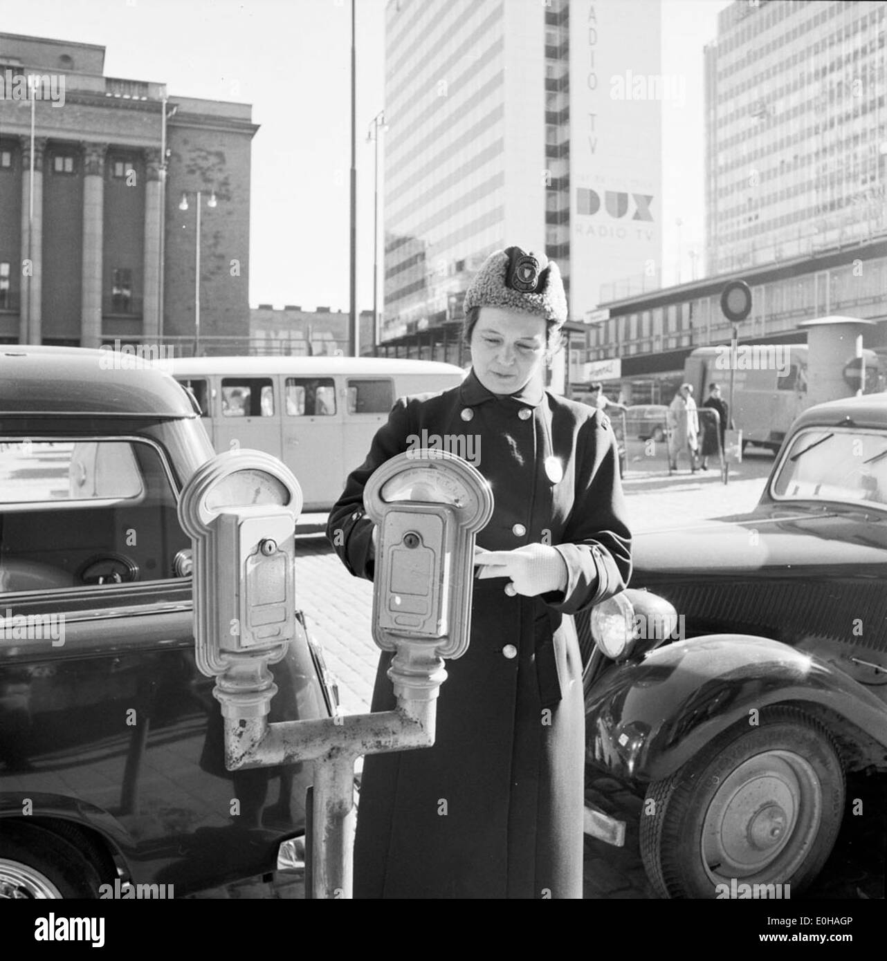 Cette image montre une femme de ménage de mètre à Stockholm en 1961. La photo capture la tâche quotidienne de billetterie des voitures garées, une scène commune dans les villes urbaines au milieu du XXe siècle, reflétant l'approche de la ville en matière de gestion du stationnement et des règles de circulation à cette époque. Banque D'Images