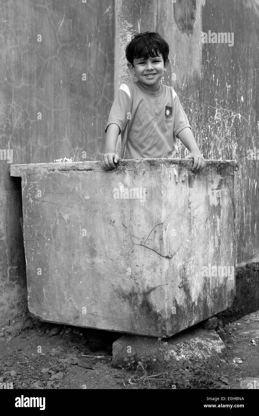 Heureux petit écolier en uniforme jouant dans une poubelle en béton sur le chemin de sa maison dans petit village rural à Java en Indonésie Banque D'Images