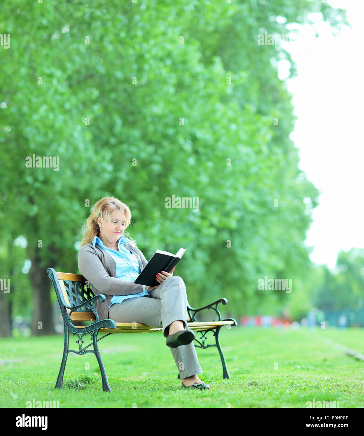 Young Woman Reading a book in park assis sur un banc en bois Banque D'Images