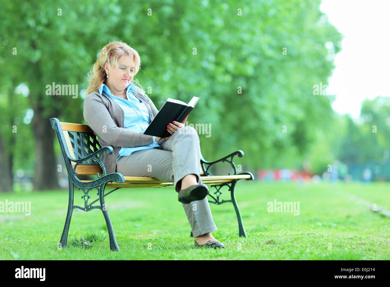 Dame mature se détendre avec un livre dans le parc assis sur banc en bois Banque D'Images