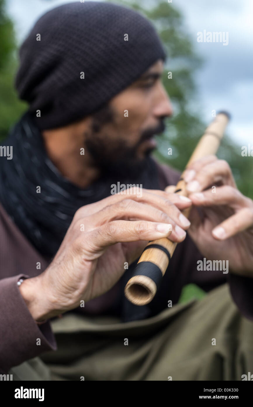 Mixed Race man playing flute dans l'herbe longue sur Hampstead Heath portant des vêtements amples et foulard Banque D'Images