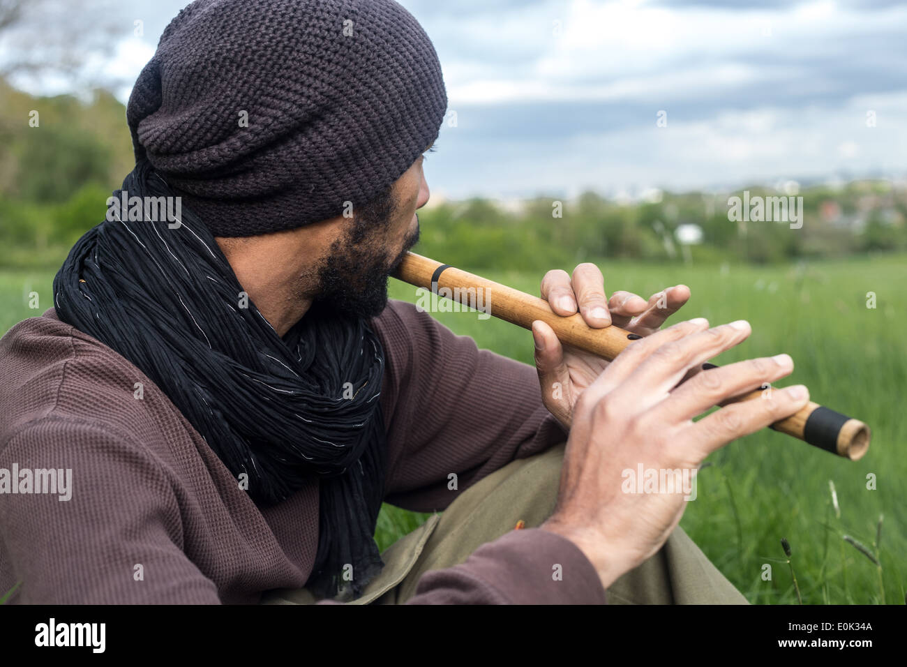 Mixed Race man playing flute dans l'herbe longue sur Hampstead Heath portant des vêtements amples et foulard Banque D'Images