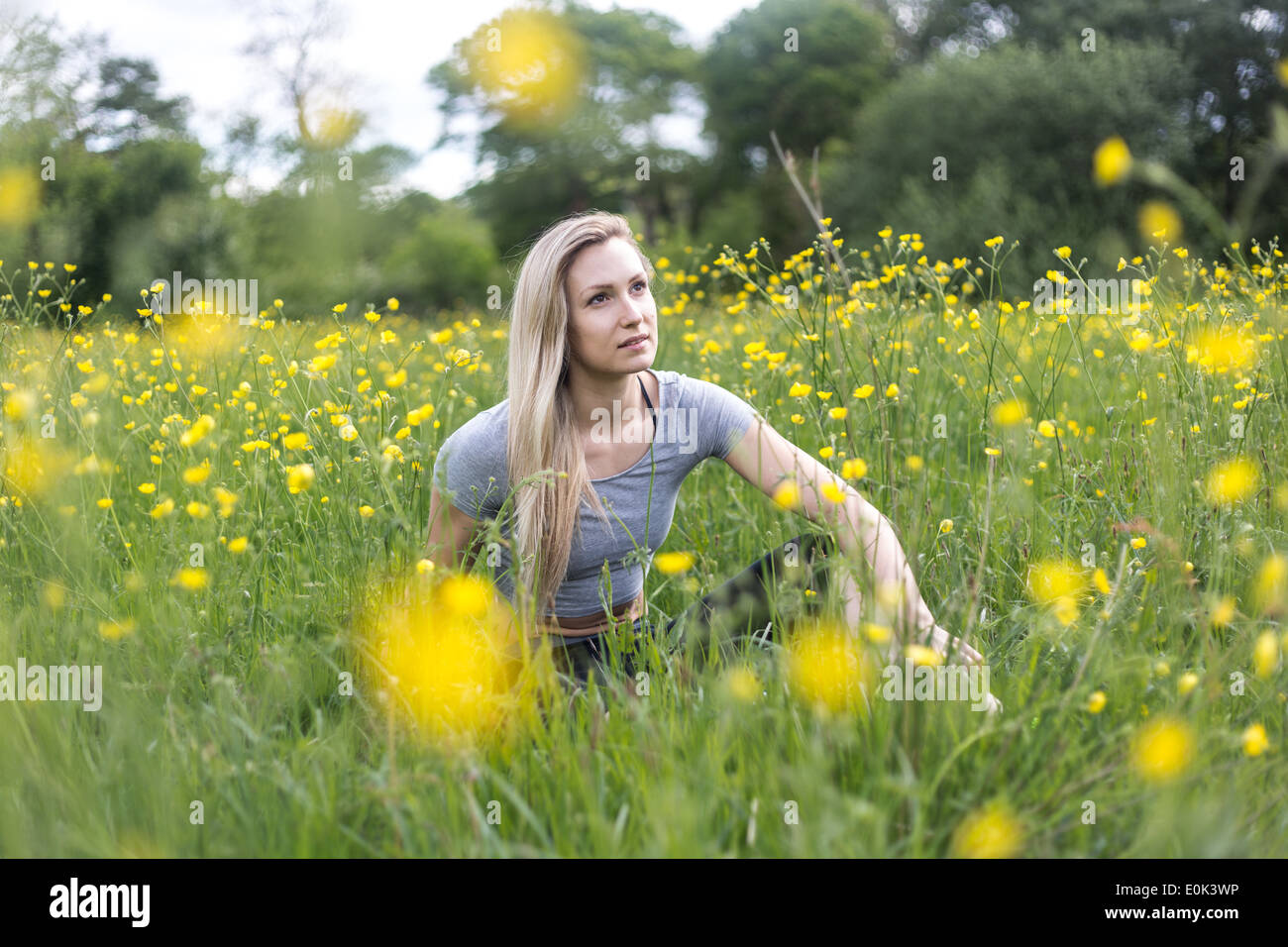 Dame blonde portant des guêtres noires et un top gris assis dans l'herbe avec des fleurs jaunes Hampstead Heath. Banque D'Images