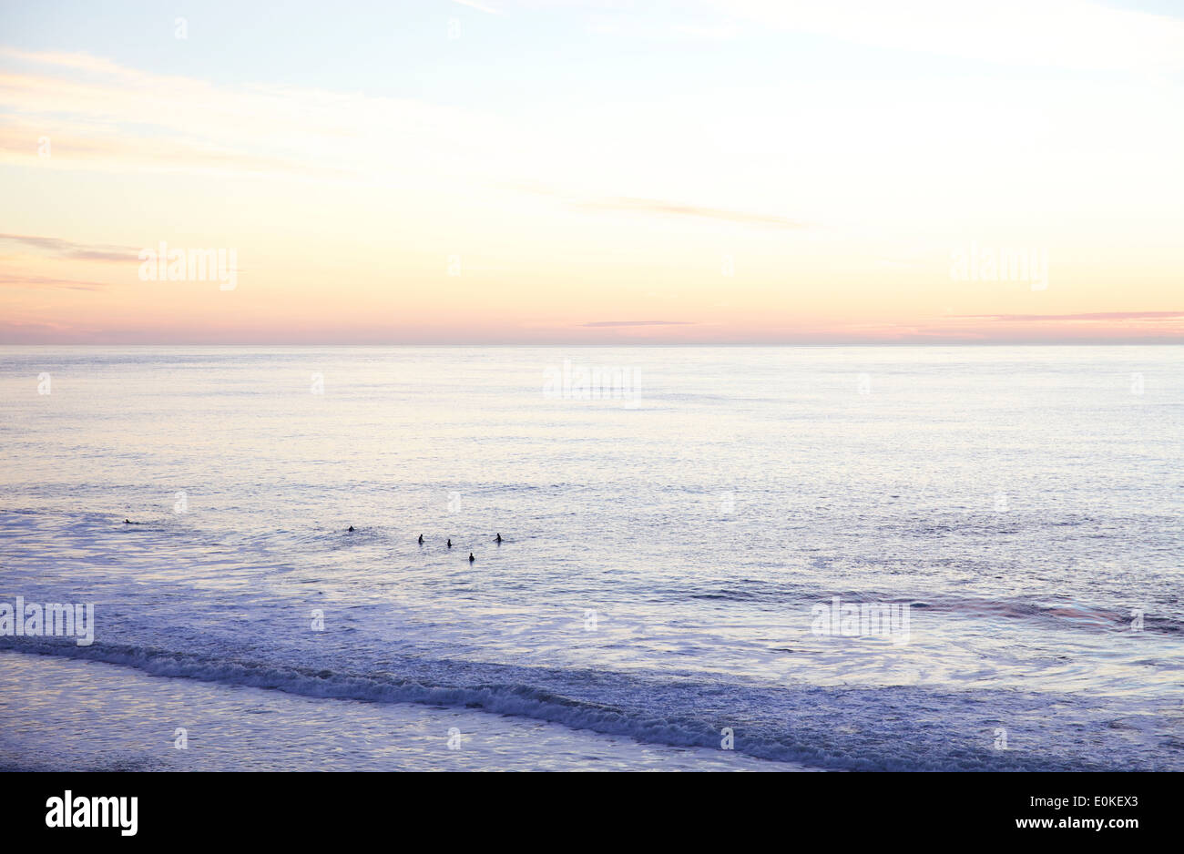 Au loin les surfeurs attendent patiemment pour attraper une vague sont découpé sur le coucher du soleil sur l'horizon. Banque D'Images