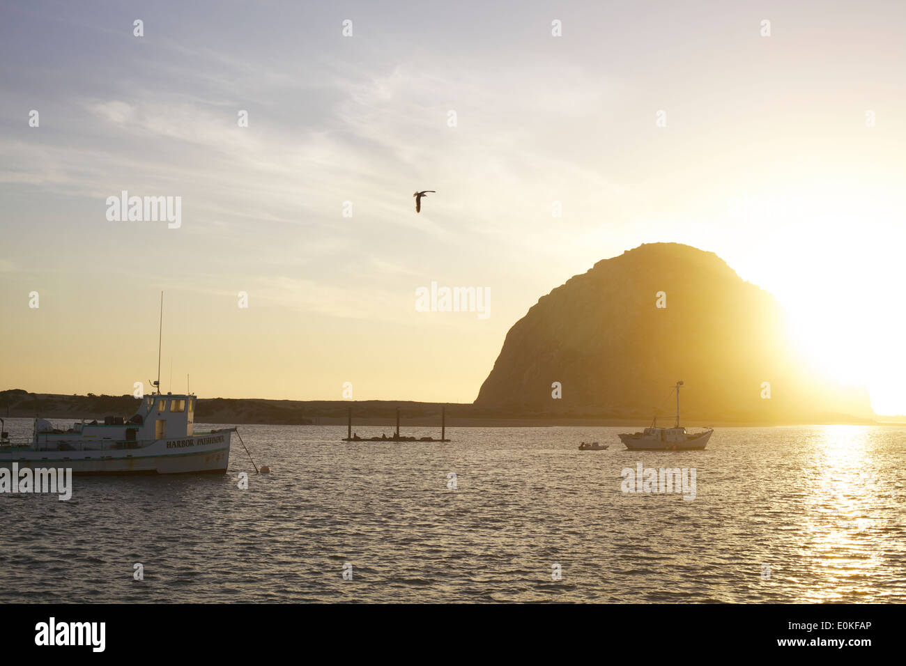 Les bateaux flottent sur l'eau comme le soleil se couche derrière la baie de Morro Rock in Morro Bay, Californie Banque D'Images