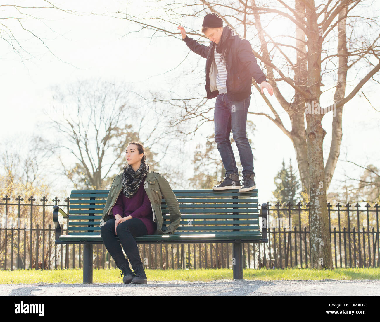 Jeune homme essayant d'impressionner indifférent girl par en équilibre sur un banc de parc. Banque D'Images