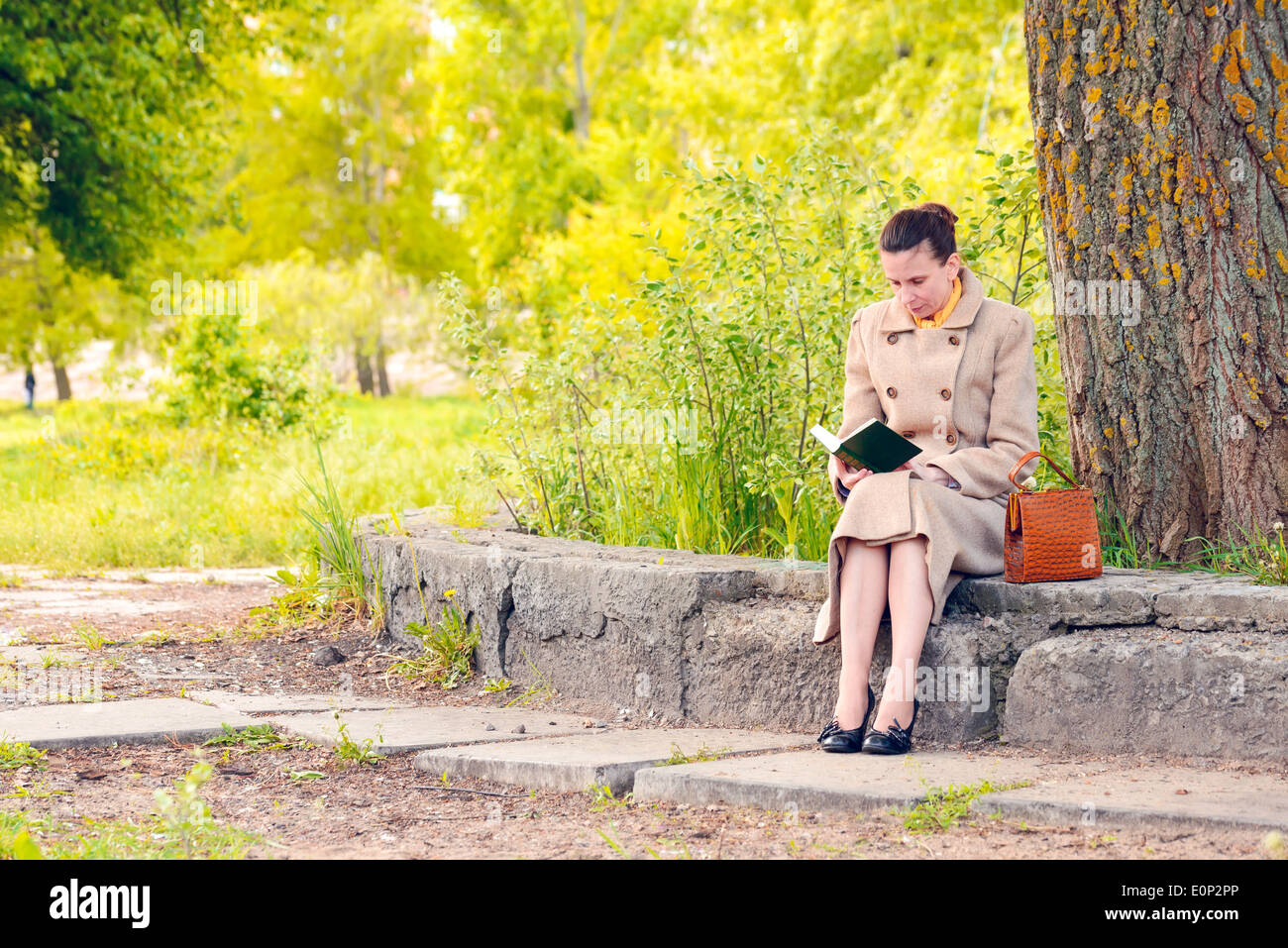 Femme élégante assise sur un mur de pierre au cours d'une journée de printemps ensoleillée, et la lecture d'un livre d'aventure Banque D'Images