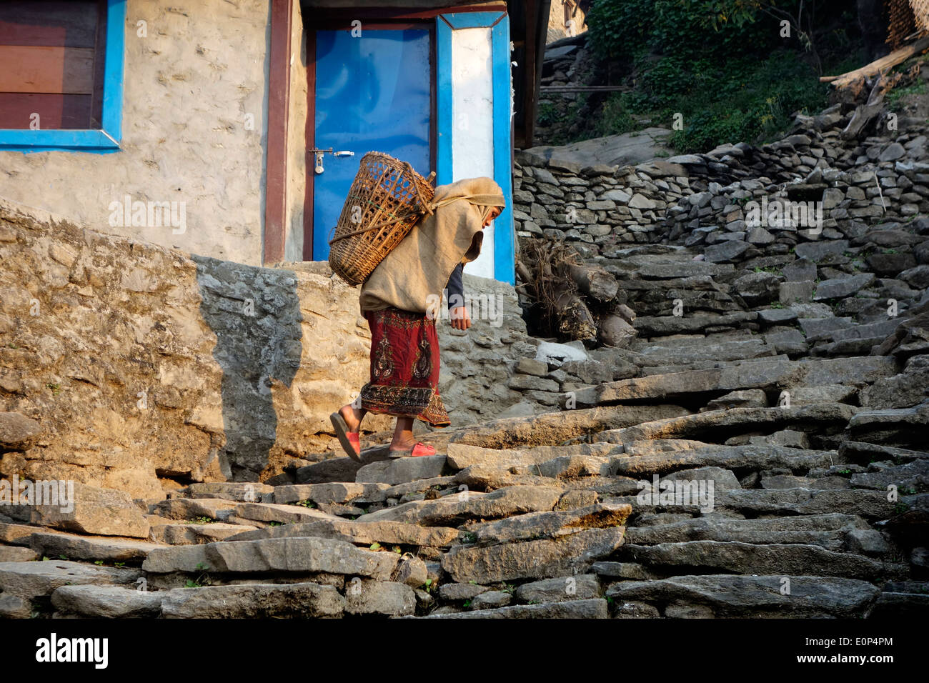 Vieille Femme escalade des marches en pierre dans village de montagne du Népal. Banque D'Images